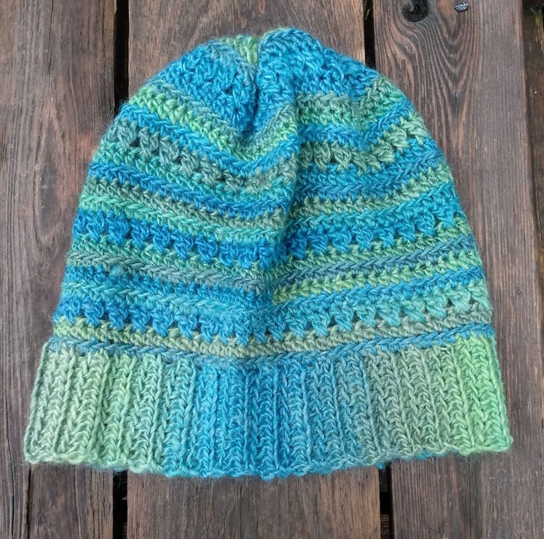 May include: A blue and green crocheted beanie hat with a striped pattern. The hat is made with a soft yarn and has a comfortable fit.