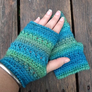 May include: A pair of crocheted fingerless gloves in shades of blue and green. The gloves have a lacy pattern and are made with a soft yarn.