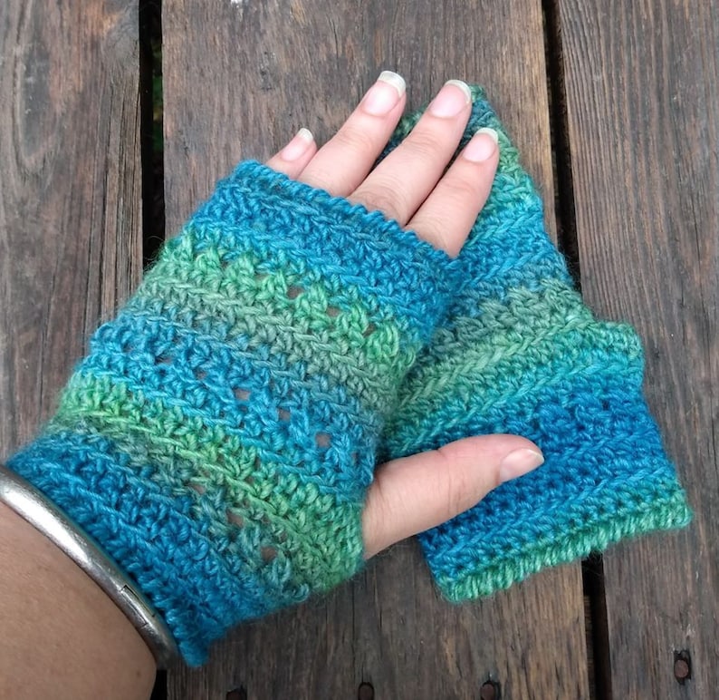 May include: A pair of crocheted fingerless gloves in shades of blue and green. The gloves have a lacy pattern and are made with a soft yarn.