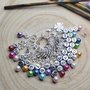 以下が含まれることがあります： カラフルなビーズが付いたシルバーのステッチマーカー10個セット。各マーカーには1から10までの番号が付けられています。マーカーは円形に配置され、ビーズは外側を向いています。ビーズは、ピンク、パープル、ブルー、グリーン、イエロー、オレンジ、レッドなど、虹色のカラーです。