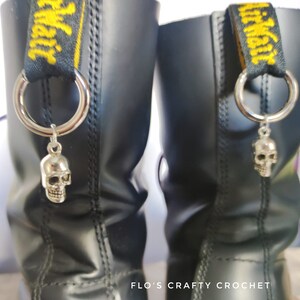 May include: A pair of black leather boots with yellow and black straps. Each strap has a silver ring with a silver skull charm attached.