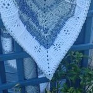 May include: A white crocheted baby blanket with a blue and white pattern. The blanket is folded and draped over a blue wooden fence.