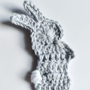 May include: A gray crocheted bunny with a white crocheted tail. The bunny is a flat, two-dimensional shape.