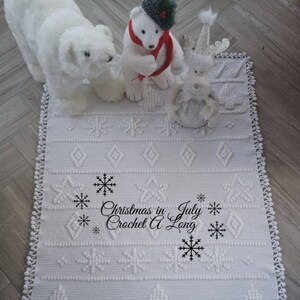 K&ouml;nnte beinhalten: Wei&szlig;er H&auml;kelteppich mit einem Schneeflockenmuster und dem Text "Christmas in July Crochet A Long" in Schwarz. Der Teppich ist mit wei&szlig;en Pl&uuml;sch-Eisb&auml;ren und einem Rentier verziert.