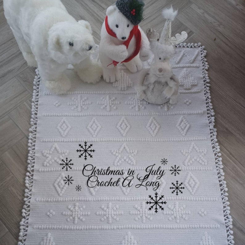 K&ouml;nnte beinhalten: Wei&szlig;er H&auml;kelteppich mit einem Schneeflockenmuster und dem Text "Christmas in July Crochet A Long" in Schwarz. Der Teppich ist mit wei&szlig;en Pl&uuml;sch-Eisb&auml;ren und einem Rentier verziert.