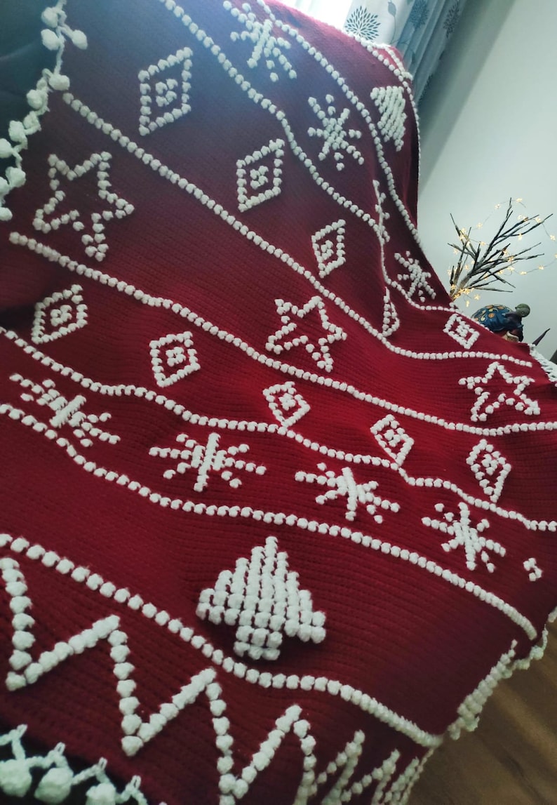 K&ouml;nnte beinhalten: Eine rote Wolldecke mit einem wei&szlig;en Schneeflocken- und Baummuster. Die Decke ist aus einem weichen, flauschigen Material gefertigt und hat eine strukturierte Oberfl&auml;che.