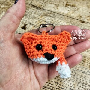 Op de afbeelding: Oranje gehaakte vos sleutelhanger met zwarte ogen en een witte neus en staart. De sleutelhanger is bevestigd aan een zilveren sleutelring.