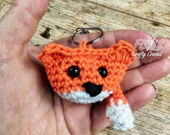 May include: Orange crocheted fox keychain with black eyes and a white nose and tail. The keychain is attached to a silver key ring.