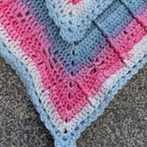 May include: A crocheted baby blanket with a pink, white and blue ombre pattern. The blanket has a delicate crocheted border.