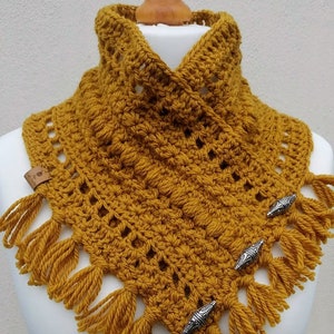 Peut inclure: Col jaune moutarde, fait au crochet, avec des franges et des fermoirs décoratifs argentés. L'écharpe de cou faite à la main présente un motif de point texturé et une petite étiquette en cuir. Cet accessoire douillet est exposé sur un mannequin.