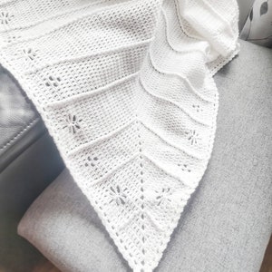 May include: White crocheted shawl with a delicate floral pattern. The shawl is draped over a grey chair.