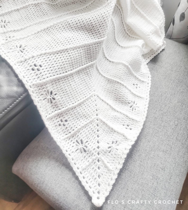 May include: White crocheted shawl with a delicate floral pattern. The shawl is draped over a grey chair.