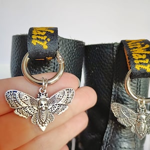 May include: A pair of black leather boots with silver skull and butterfly charms attached to the laces. The charms are hanging from silver rings.