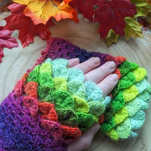Könnte beinhalten: Gehäkelte Fingerhandschuhe mit einem Drachenschuppenmuster. Die Handschuhe zeigen einen Farbverlauf von Lila nach Grün, mit orangefarbenen und roten Akzenten. Der Text "FLO'S CRAFTY CROCHET" ist sichtbar.
