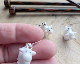 May include: Three white crocheted sheep earrings with silver ear wires. The sheep are standing on a wooden surface.