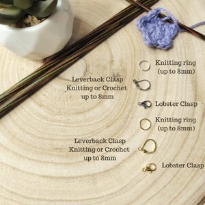 Pu&ograve; includere: Primo piano di marcatori di punto con diversi fermagli, tra cui fermagli a leva e fermagli a moschettone. Il testo recita "Stitch Marker Fastenings", "Leverback Clasp Knitting or Crochet up to 8mm", "Knitting ring (up to 8mm)", "Lobster Clasp", "Silver or Gold options available", e "FLO'S CRAFTY CROCHET".
