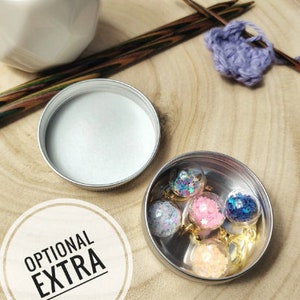 Pu&ograve; includere: Una piccola scatola di metallo con un coperchio, contenente cinque ornamenti di vetro trasparente riempiti di glitter colorati. La scatola &egrave; etichettata "EXTRA OPZIONALE".