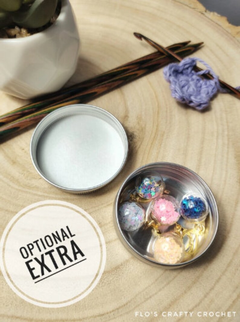 Pu&ograve; includere: Una piccola scatola di metallo con un coperchio, contenente cinque ornamenti di vetro trasparente riempiti di glitter colorati. La scatola &egrave; etichettata "EXTRA OPZIONALE".