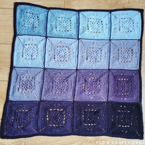 May include: A crocheted blanket with a gradient of blue and purple squares. The blanket is made with a delicate stitch pattern and has a black border.