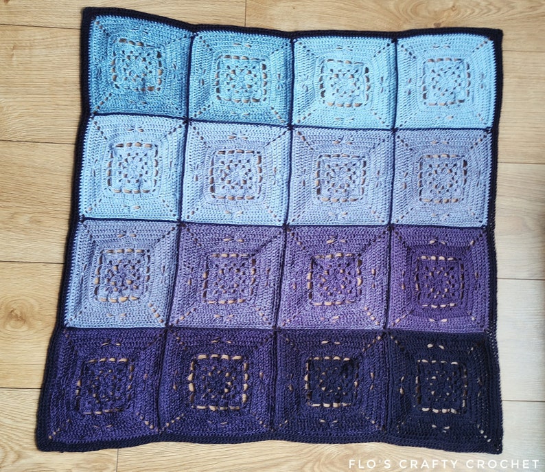 May include: A crocheted blanket with a gradient of blue and purple squares. The blanket is made with a delicate stitch pattern and has a black border.