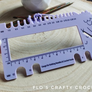 May include: Purple plastic gauge for knitting needles and crochet hooks with a ruler in millimetres and centimetres. The gauge has a cutout in the shape of a horse's head with the text "FLO'S CRAFTY CROCHET" printed below.
