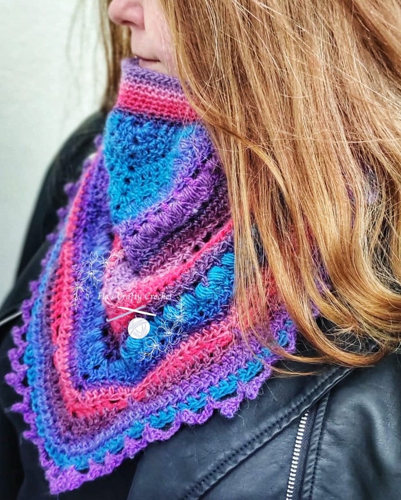 Peut inclure: Un col crochet&eacute; color&eacute; dans les tons de violet, rose et bleu. L'&eacute;charpe faite &agrave; la main pr&eacute;sente un bord festonn&eacute; et une fermeture boutonn&eacute;e. Le col est port&eacute; sur une veste noire.