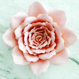 May include: A large, blush pink paper flower with multiple layers of petals. The flower is made of paper and has a delicate, feminine look.