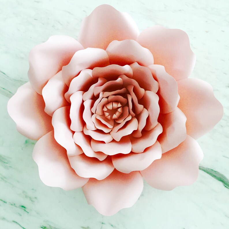 May include: A large, blush pink paper flower with multiple layers of petals. The flower is made of paper and has a delicate, feminine look.