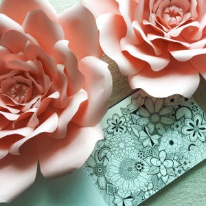 May include: Two large, pink paper flowers with a black and white intricate floral design on a white background.