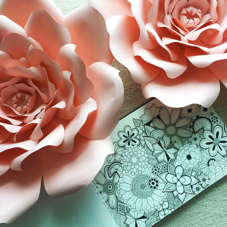 May include: Two large, pink paper flowers with a black and white intricate floral design on a white background.