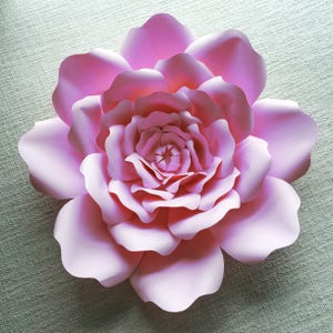 May include: A large, pink paper flower with multiple layers of petals. The flower is made of paper and has a delicate, feminine look.