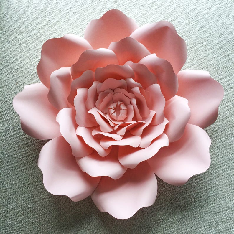 May include: A large, pink paper flower with multiple layers of petals. The flower is made of paper and has a delicate, feminine look.