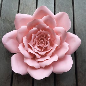 May include: A large, pink paper flower with multiple layers of petals. The flower is made of paper and has a delicate, feminine look.