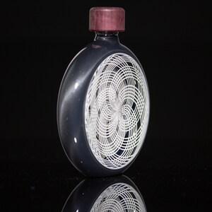 May include: A dark gray glass bottle with a white geometric design on the front. The bottle has a dark wood top.