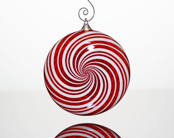 May include: A round, red and white striped glass bauble with a spiral design. The bauble has a reflective surface and is suspended by a wire hook. The design resembles a peppermint candy. Christmas decor.