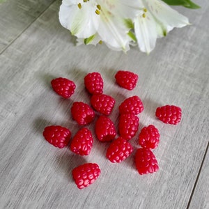 May include: A group of 14 red raspberries on a light gray wooden surface. The raspberries are arranged in a loose cluster, with some overlapping.