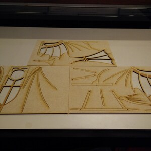 May include: Four pieces of laser-cut wood with intricate designs, likely for a model or craft project. The pieces feature a repeating pattern of curved lines and geometric shapes.