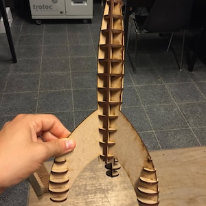Puede incluir: Un modelo de cohete de madera con un diseño detallado y en capas. El modelo está hecho de varias piezas de madera que se unen para crear una forma tridimensional. El cohete está pintado en un color madera natural.