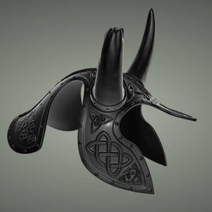 Puede incluir: Un casco negro con cuernos y dise&ntilde;os intrincados de nudos celtas. El casco est&aacute; hecho de metal y tiene una superficie texturizada.