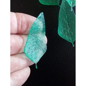 May include: A set of five green translucent leaf-shaped resin embellishments. The leaves are approximately 5 cm long and have a textured surface.
