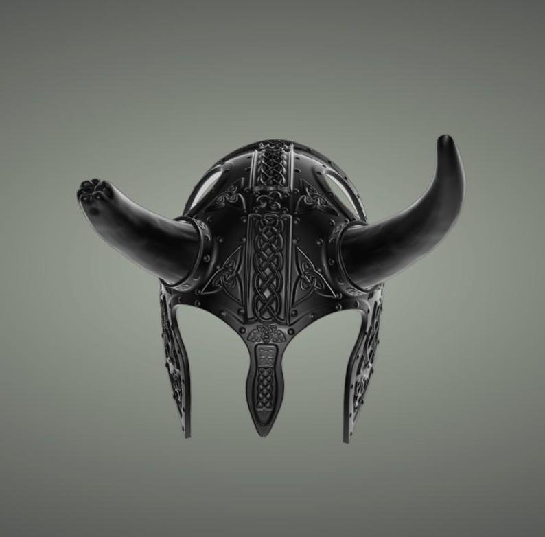 Puede incluir: Un casco vikingo negro con cuernos y detalles intrincados de metal. El casco tiene un dise&ntilde;o de nudo celta y est&aacute; hecho de metal.