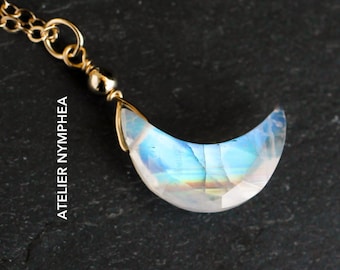 Puede incluir: Un collar de cadena dorada con un colgante de media luna hecho de piedra de luna arcoíris iridiscente.