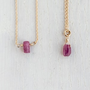 Könnte beinhalten: Zwei goldene Halsketten mit rosafarbenen Edelsteinanhängern. Eine Halskette hat einen rechteckigen Anhänger und die andere einen tropfenförmigen Anhänger.