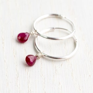 Può includere: Orecchini a cerchio in argento con pendenti di pietre preziose rosso rubino.