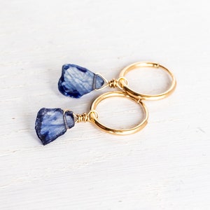 May include: A pair of gold hoop earrings with blue gemstone dangles. The gemstones are irregular in shape and have a cloudy, translucent appearance.