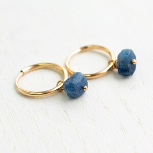 Könnte beinhalten: Ein Paar goldene Creolen mit einem blauen Edelstein, der an jeder Creole baumelt.
