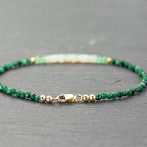 Puede incluir: Una pulsera delicada con peque&ntilde;as cuentas facetadas de color verde oscuro y una fila central de cuentas blanquecinas iridiscentes. El dise&ntilde;o est&aacute; acentuado con diminutas esferas met&aacute;licas doradas y un cierre de mosquet&oacute;n dorado.