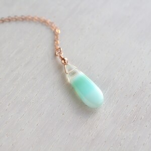 May include: A necklace featuring a teardrop-shaped pendant with a smooth, opaque mint green base that transitions into a translucent, clear top section. The pendant is suspended from a delicate rose gold-toned metal chain by a small wire-wrapped loop.