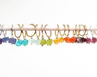 Könnte beinhalten: Ein Set mit 12 Paaren goldener Creolen mit verschiedenen bunten Edelstein-Anhängern. Die Anhänger sind in den Farben Lila, Blau, Grün, Gelb, Orange, Rot und Pink.