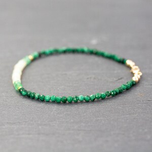 Puede incluir: Una delicada pulsera de cuentas con peque&ntilde;as piedras facetadas de color verde oscuro, una secci&oacute;n corta de cuentas de color crema claro y un peque&ntilde;o cierre de metal dorado. Las cuentas est&aacute;n dispuestas en c&iacute;rculo, mostrando un degradado.
